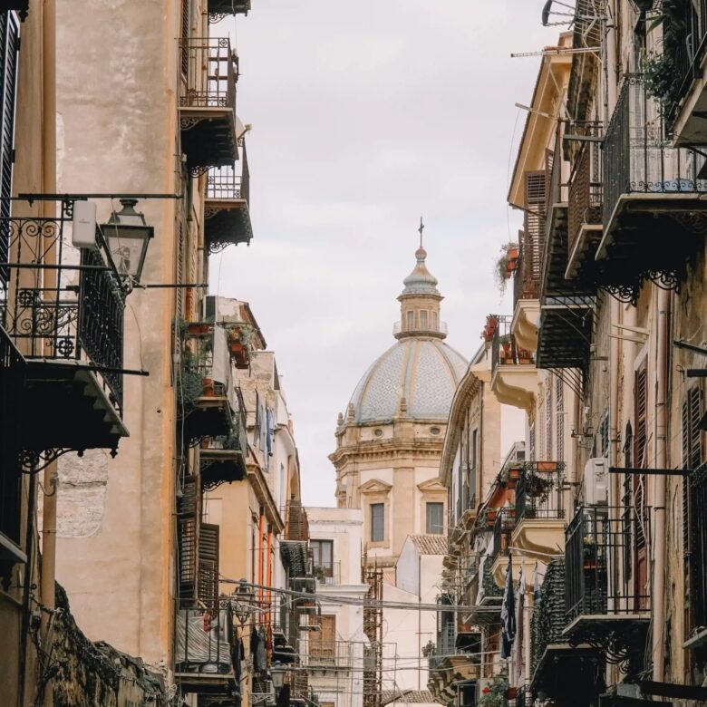 Vicolo del centro storico di Palermo, con balconi in ferro battuto e la cupola maiolicata di una chiesa barocca sullo sfondo
